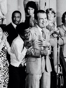 Entertainer Sammy Davis Jr., grabs President Nixon from behind and squeezes his arms while Nixon talks to about 8,000 of his youthful supporters in a youth rally August 22, 1972. Davis' spontaneous gesture came shortly after the President had been nominated for reelection by the Republican National Convention. (AP Photo/Jim Palmer)